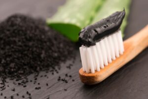 Closeup of a bamboo toothbrush with black toothpaste on it with a pile of charcoal in the background